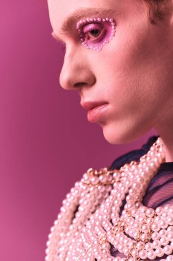 A person displays pride with vibrant makeup and trendy clothing in an artsy setting.