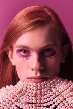 Person embodies pride and creativity with unique makeup, styled hair, and an artistic collar.