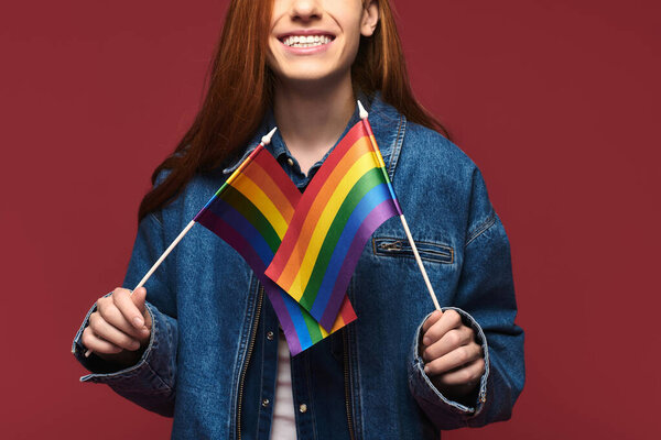A joyful person holds rainbow flags, representing love and acceptance, by a colorful wall.