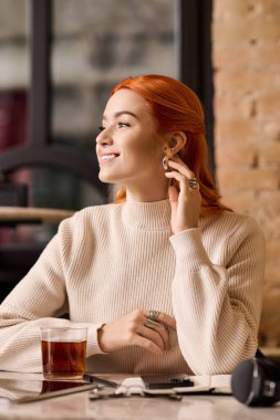 Canlı kızıl saçlı güzel bir kadın rahat rahat oturur, şık bir kafede çayını yudumlar..