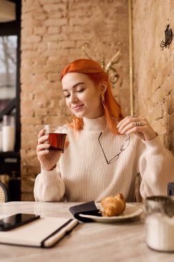 Canlı kızıl saçlı genç bir kadın modern bir kafede oturup çayının tadını çıkarıyor..
