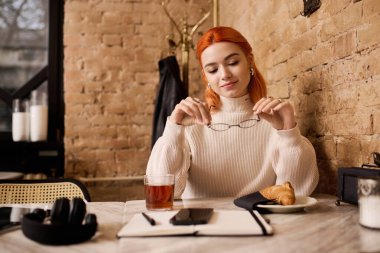 Şık bir kafede oturan, ateşli kızıl saçlı genç bir kadın çayını yudumluyor, pastanın tadını çıkarıyor..