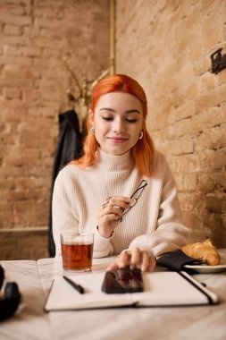 Kızıl saçlı genç bir kadın bir kafede içkisini yudumlarken notlarını gözden geçiriyor..