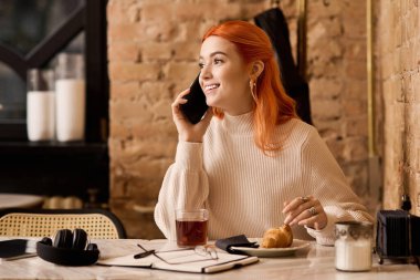 Neşeli genç bir kadın, canlı kızıl saçlarıyla telefonda sohbet ediyor..