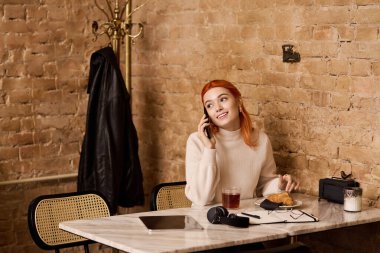 Şık bir kafede çerez yerken telefonda konuşan kızıl saçlı genç bir kadın..