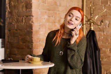 Canlı, genç bir kadın, modern bir kafede içkisini yudumlarken telefonda kızıl saçlı sohbet ediyor..