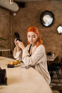 Kızıl saçlı güzel bir kadın modern bir kafede dinleniyor, yemek ve içkilerinin tadını çıkarıyor..