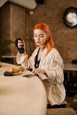 Moda bir kafede, kızıl saçlı genç bir kadın kahve, pasta ve müzikle rahatlıyor..