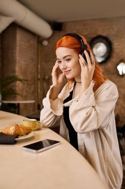 Canlı kızıl saçlı genç bir kadın son moda bir kafede müzik dinlerken dinleniyor..