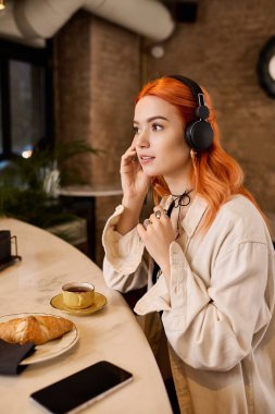 Canlı, kızıl saçlı genç bir kadın şık bir kafede oturup içkisinin tadını çıkarıyor..