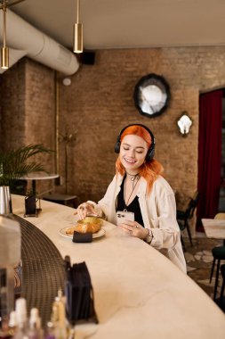 Kızıl saçlı genç bir kadın şık bir kafede gevşiyor, atıştırmalık ve müziğin tadını çıkarıyor..