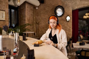 Canlı kızıl saçlı genç bir kadın modern bir kafede dinleniyor, yemek ve müziğin tadını çıkarıyor..