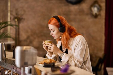 Kızıl saçlı genç bir kadın şık bir kafede müzik dinlerken kahvesini yudumluyor..