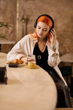 Güzel kızıl saçlı genç bir kadın modern bir kafede dinleniyor, kahve ve müziğin tadını çıkarıyor..