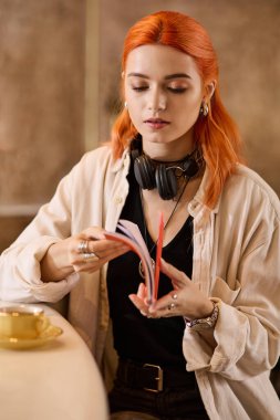 Canlı kızıl saçlı genç bir kadın modern bir kafede dinlenirken kitap okuyor..