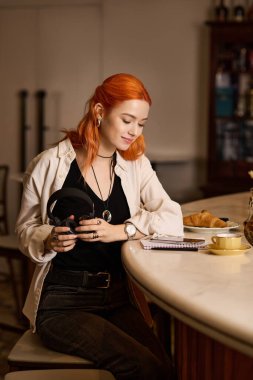 Kızıl saçlı genç bir kadın bir kafede dinleniyor, yazarken kahvesinin tadını çıkarıyor..