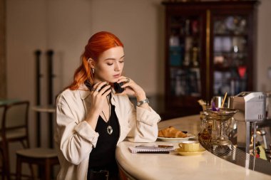 Kızıl saçlı güzel bir kadın, pastalarla çevrili sıcacık bir kafede sessizce yansıyor..