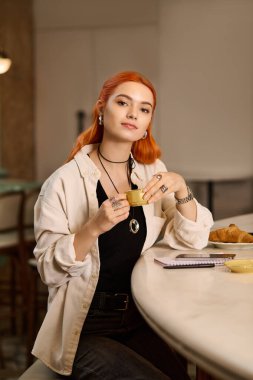 Parlak kızıl saçlı kadın moda bir kafede rahatça otururken kahvesini yudumluyor..