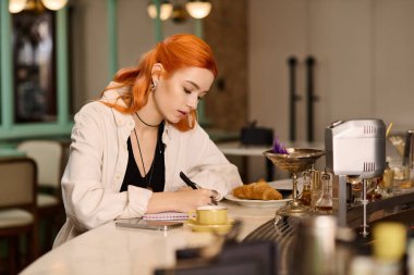 Kızıl saçlı güzel bir kadın, kahve yudumlarken defterine bir şeyler yazıyor..