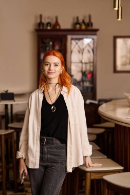 Kızıl saçlı, kendine güvenen genç bir kadın modern bir kafede şık duruyor..