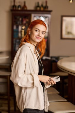 Canlı kızıl saçlı genç bir kadın modaya uygun bir kafede eğleniyor, pozitif enerji saçıyor..