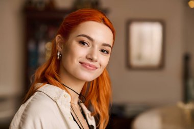 Parlak, modern bir kafede, çarpıcı kızıl saçlı genç bir kadın sıcacık gülümser, mutluluk saçar..