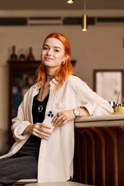 Kızıl saçlı güzel bir kadın modern bir kafede rahatça gülümseyip poz veriyor..