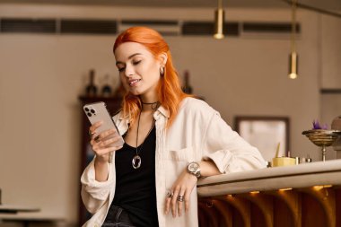 Kızıl saçlı, mutlu genç bir kadın telefonunu kontrol ederken şık bir kafede rahatlıyor..