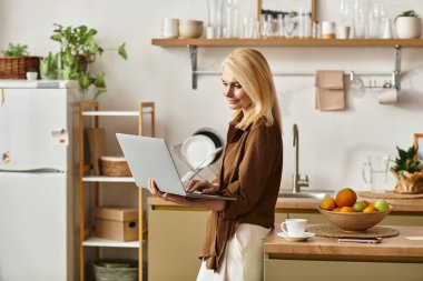 Kıdemli kadın kahvaltıdan zevk alıyor ve sevdikleriyle parlak bir mutfakta dizüstü bilgisayarında bağlantı kuruyor..