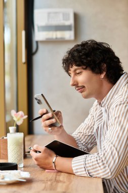 Bir kafedeki genç adam yazar, telefonuna gülümser ve bir şeyler içer..