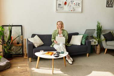 Parlak, rahat bir yerde koltukta dinlenen ve evdeki kağıtlarla uğraşan bir kadın var..