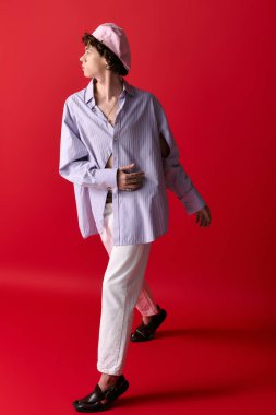 Genç adam modern modayı gösterip, gösterişli bir şekilde kırmızı duvarın önünde poz veriyor..