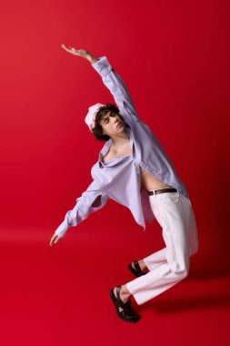 Şık bir genç adam neşeli bir şekilde kırmızı bir arka plana karşı poz verir..