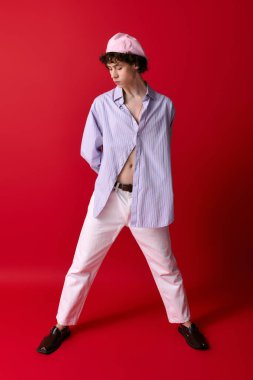 Genç adam benzersiz tarzını, çarpıcı kırmızı bir ortamda neşeli bir pozla sergiliyor..