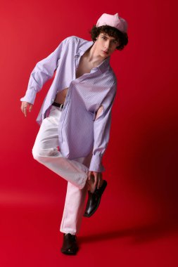 Moda kıyafetli genç adam kırmızı bir arka plana karşı poz veriyor, tarzını gösteriyor..