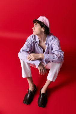 Genç, yakışıklı bir adam kendine güvenerek yerde poz veriyor, modaya uygun kıyafetler ve eşsiz bir tarz sergiliyor..