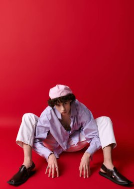 Modern kıyafetli genç bir adam eşsiz bir poz sergiliyor. Cesur kırmızı karşısında sanatsal yeteneğini sergiliyor..