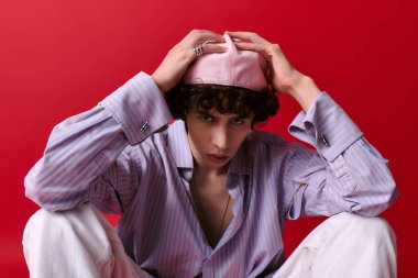 Şık bir genç adam kırmızı arka planda oturuyor, şapkasını düzeltiyor..