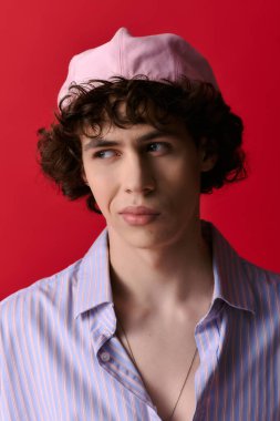 Kendine güvenen, modaya uygun kıyafetler giyen ve pembe şapkalı genç bir adam dinamik kırmızı bir zemin üzerinde duruyor..