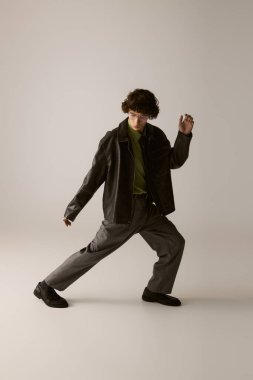 Şık giyinmiş genç adam, minimalist bir zeminde dinamik bir poz veriyor..