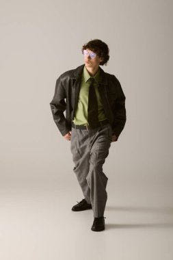 Yakışıklı genç adam, stüdyo ortamında kendine güven ve tarzını somutlaştırırken modaya uygun kıyafetler sergiliyor