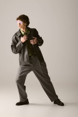 Genç bir adam dikkat çekici bir şekilde dikiliyor, terzi kıyafeti içinde, şık bir çekiciliği ve güveni var..