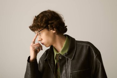 Yakışıklı, modaya uygun giyinmiş genç bir adam. Tarafsız bir arkaplana karşı düşünceli bir şekilde poz veriyor..