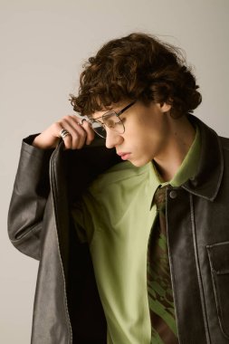 Tarz sahibi genç bir adam, tarafsız bir arkaplanda düşünceli bir poz verir..