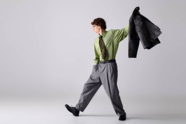 Sivri giyinmiş genç bir adam elinde ceketle şık bir poz veriyor..