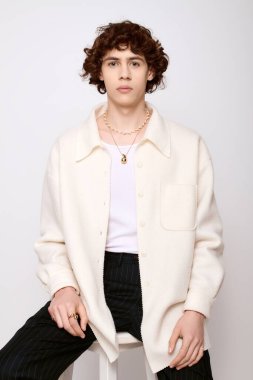 Yakışıklı genç adam zarif pozlar veriyor, şık kıyafetini sade bir arkaplanda sergiliyor..