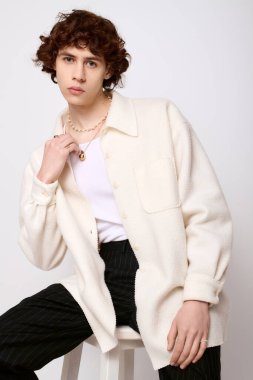 Yakışıklı genç bir adam basit bir arkaplana karşı rahat bir pozla şık bir kıyafet sergiliyor.