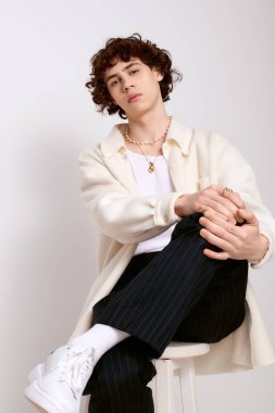 Genç, yakışıklı bir adam, modaya uygun giyinmiş bir şekilde, bir taburede otururken tarz yayar..