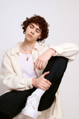 Yakışıklı, modaya uygun giyinmiş genç adam düşünceli bir şekilde oturuyor ve eşsiz tarzını sergiliyor..