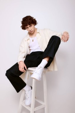 Yakışıklı genç adam bir taburede rahatça otururken modaya uygun giysiler sergiliyor..